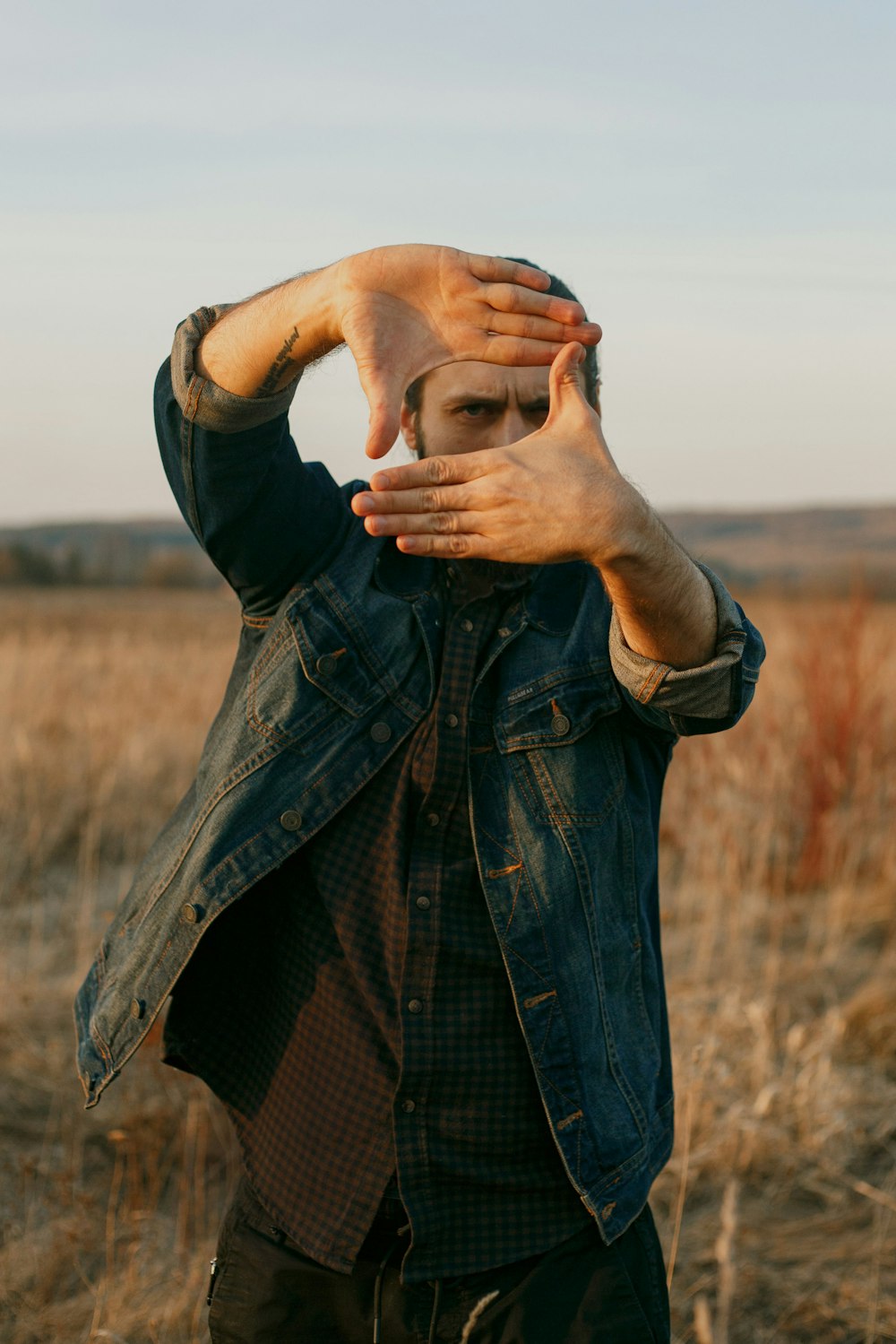 man in blue denim button up jacket covering his face with his hand