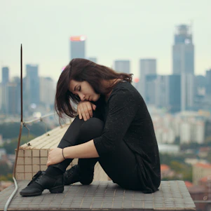 A young adult sitting thoughtfully on a city rooftop at sunset, symbolizing the weight of life's uncertainties.