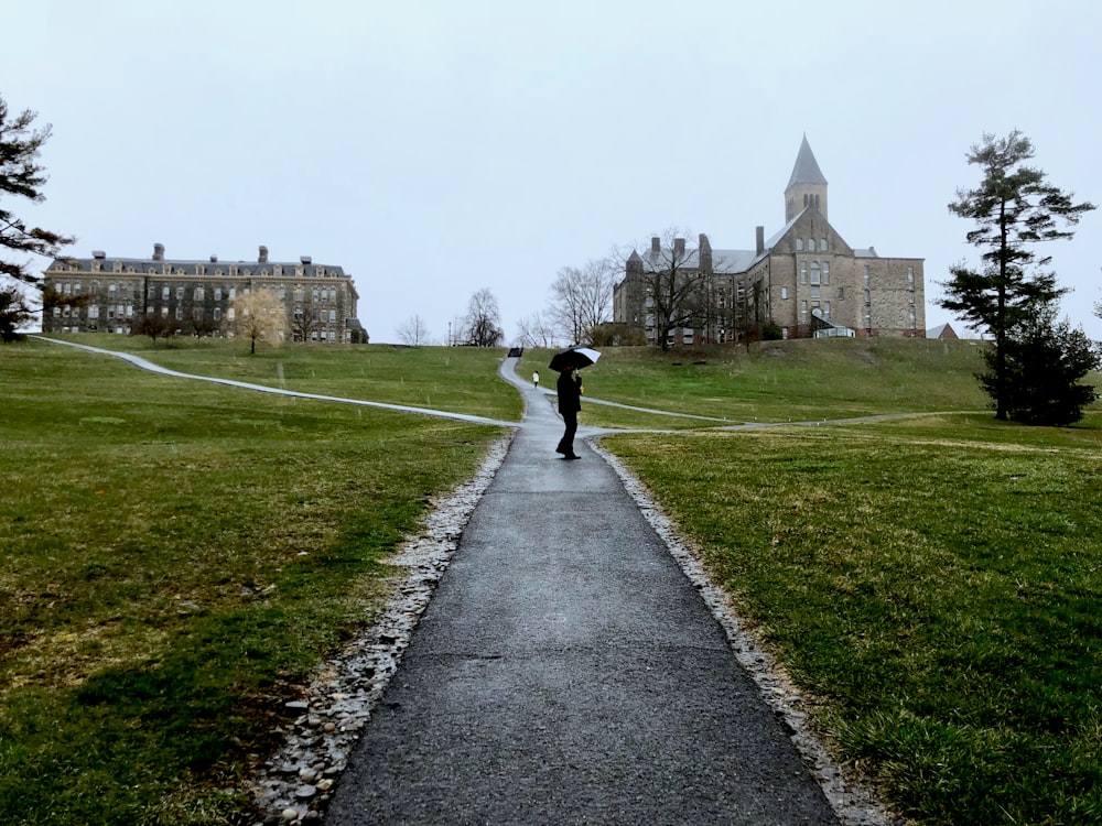 person walking on pathway near green grass field during daytime