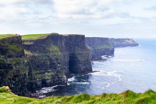green and gray cliff beside sea under white clouds during daytime in County Clare Ireland
