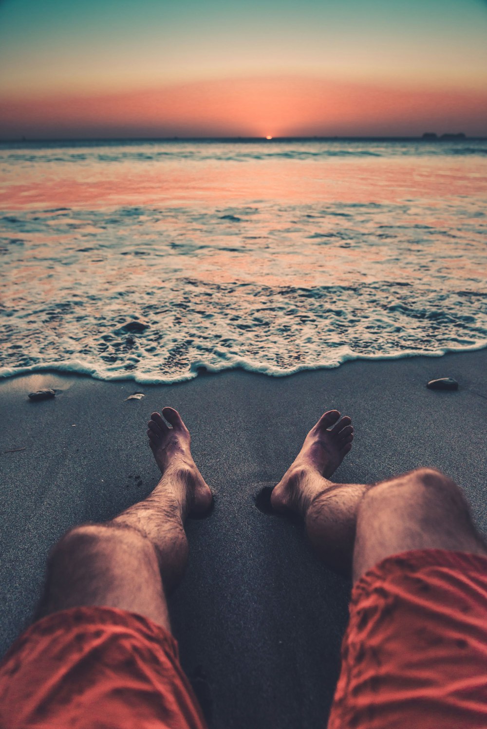 persona in pantaloncini rossi che si siede sulla spiaggia durante il giorno