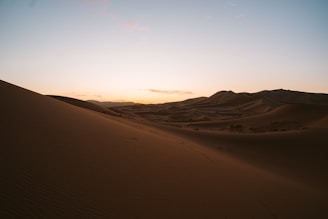 A quiet desert landscape with soft dunes under a vast, pastel-colored sky.