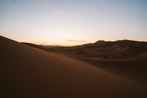 A quiet desert landscape with soft dunes under a vast, pastel-colored sky.