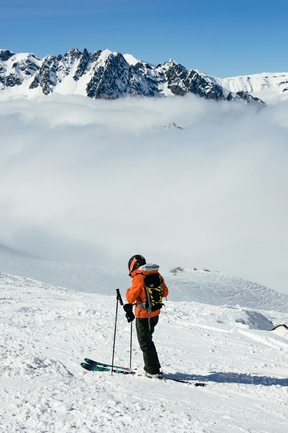 man in orange jacket and black pants standing on snow covered ground