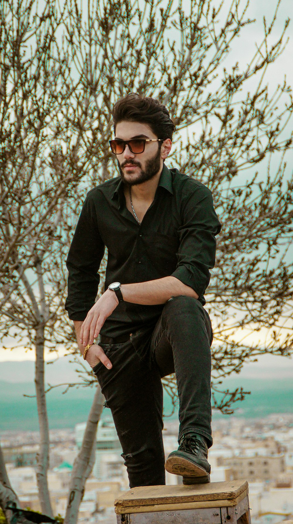 man in black dress shirt and blue denim jeans sitting on brown wooden bench during daytime