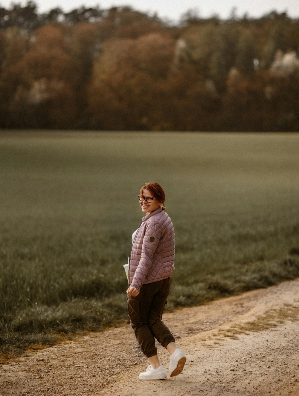 Chica con sudadera con capucha rosa parada en un camino de tierra marrón durante el día