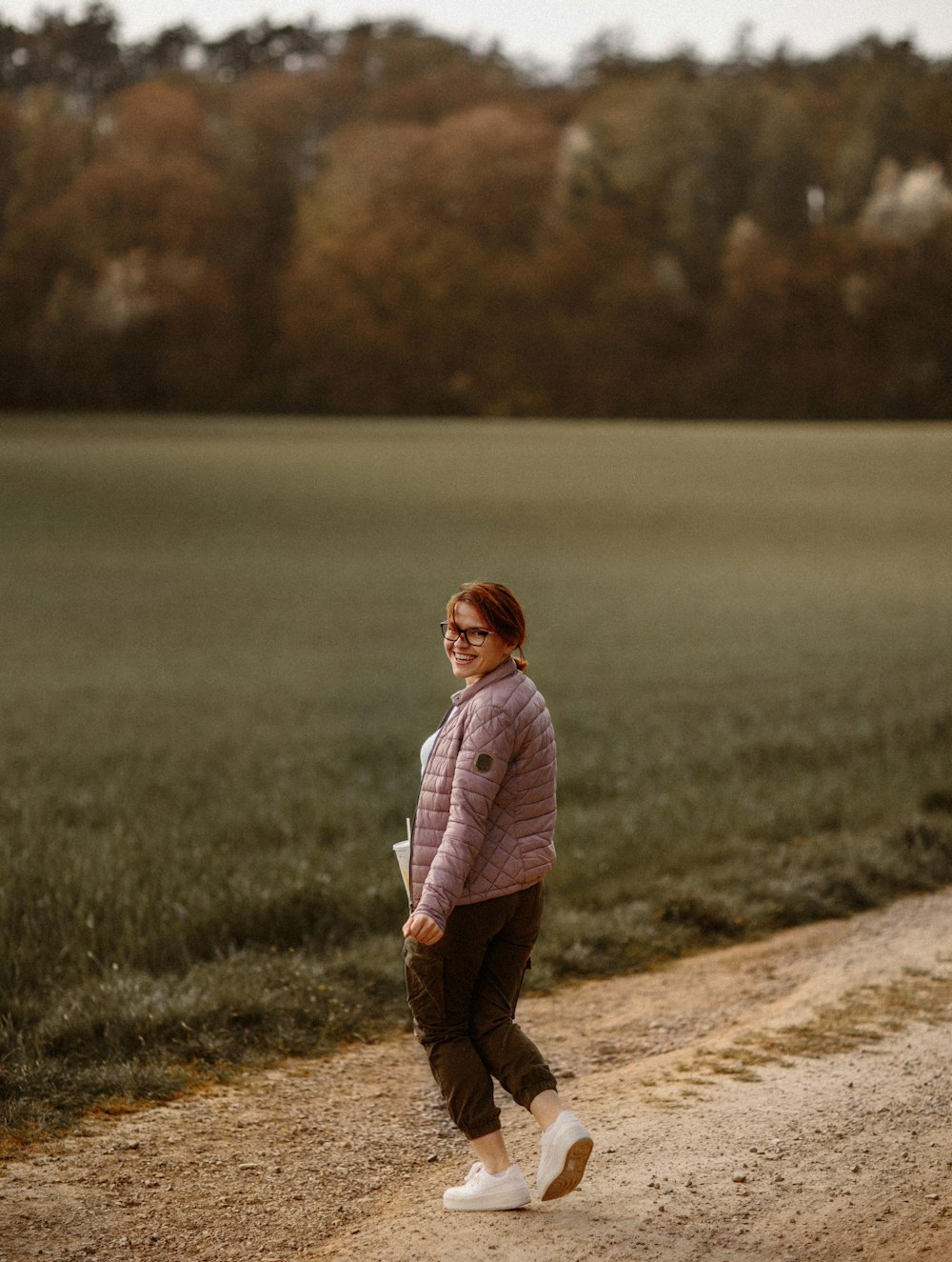 Ragazza in felpa rosa con cappuccio in piedi sulla strada sterrata marrone durante il giorno