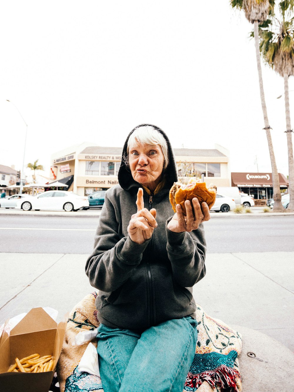man in black leather jacket and blue denim jeans sitting on sidewalk while holding brown bread