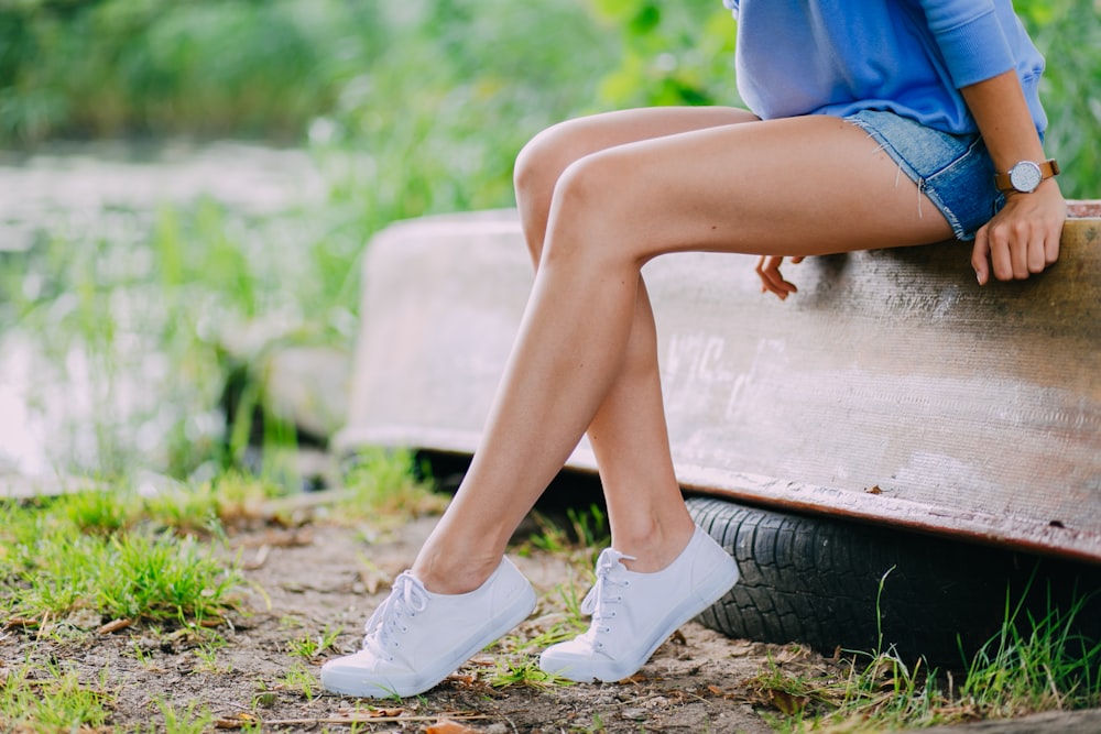 woman in blue denim shorts and white nike sneakers sitting on brown wooden bench