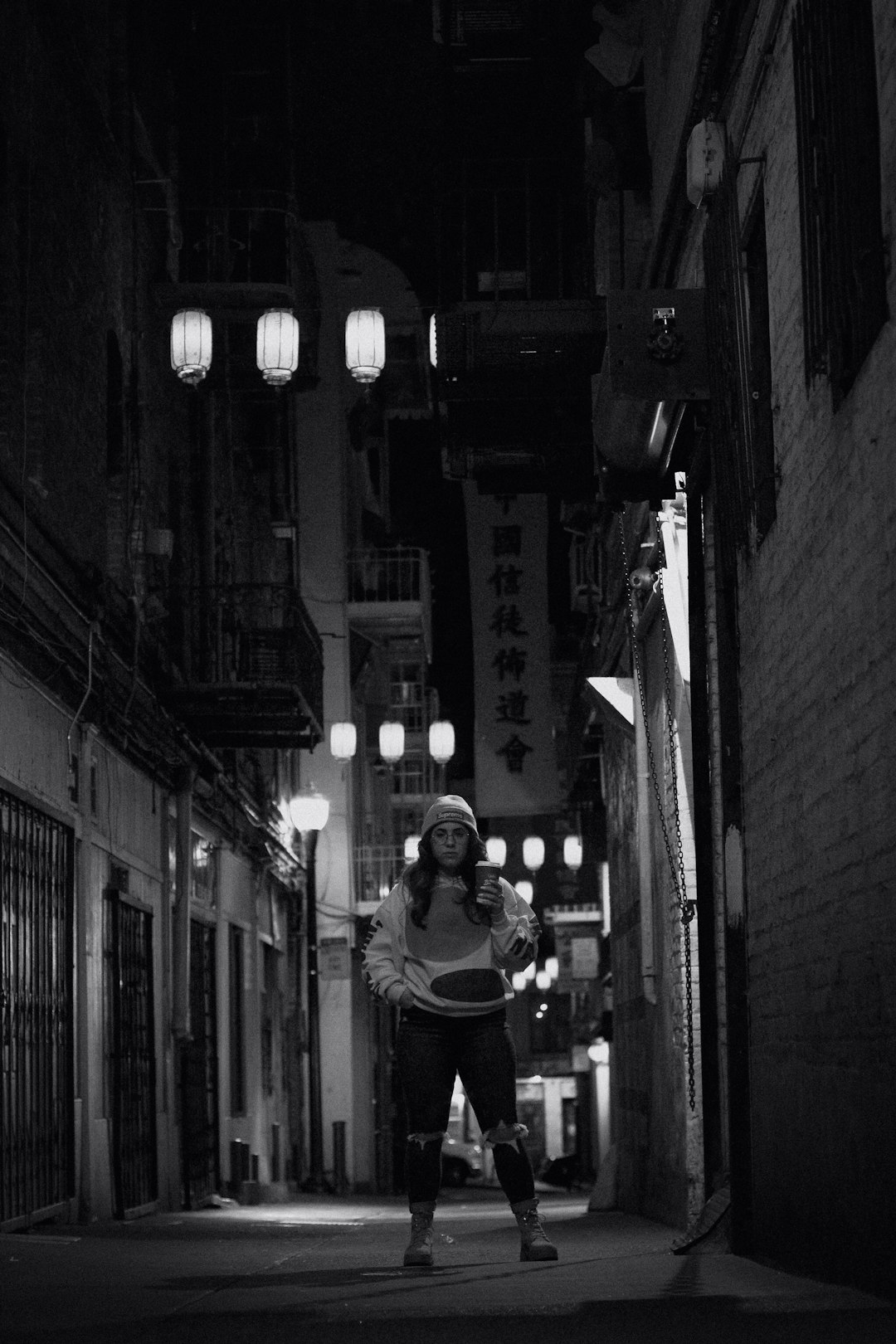 grayscale photo of woman in black long sleeve shirt and pants standing on sidewalk