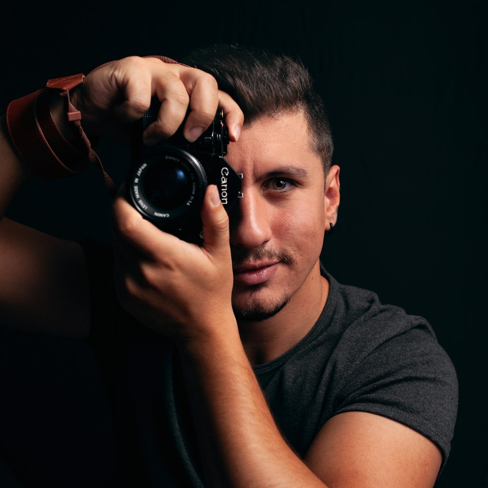 man in gray crew neck t-shirt holding black dslr camera