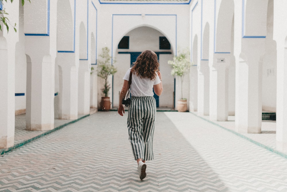 woman in white shirt and black and white skirt walking on sidewalk during daytime