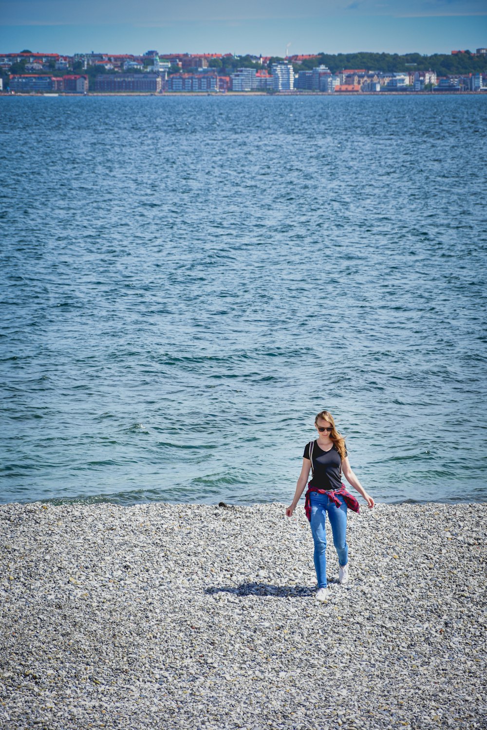 woman in black tank top and blue denim jeans standing on gray sand near body of near near near near