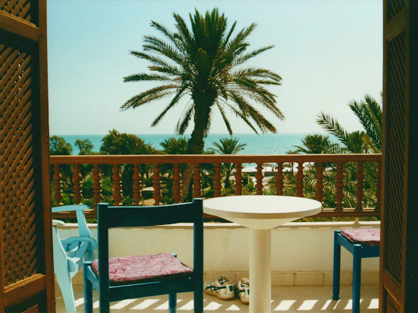 Private balcony with a small table and chairs, framed by palm trees and ocean breeze.