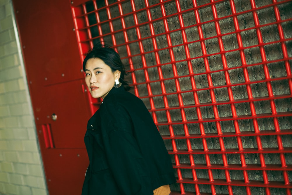 woman in black coat standing beside red wall