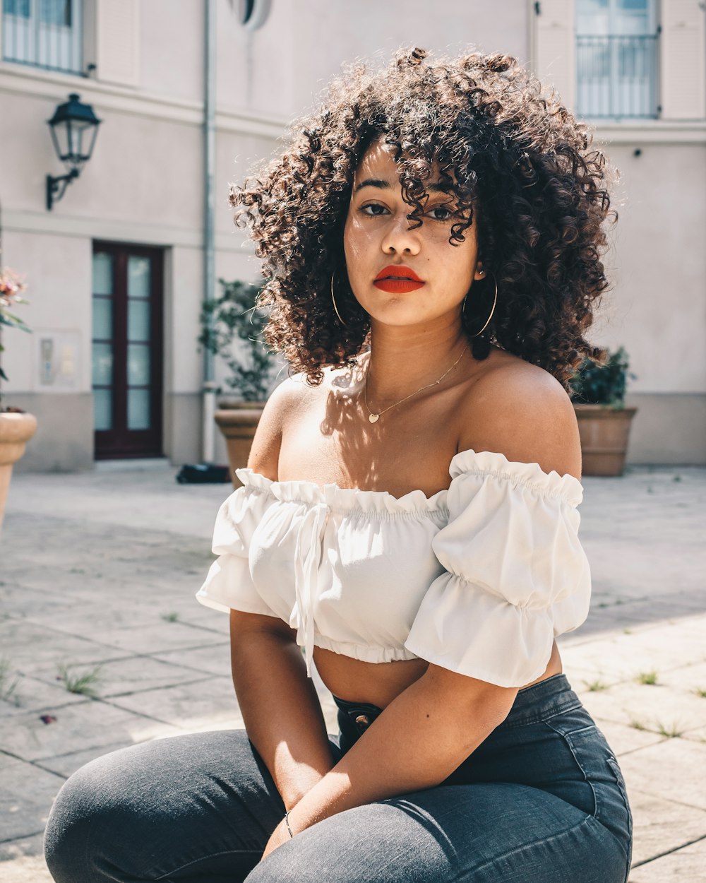 woman in white off shoulder shirt and blue denim shorts sitting on concrete bench during daytime