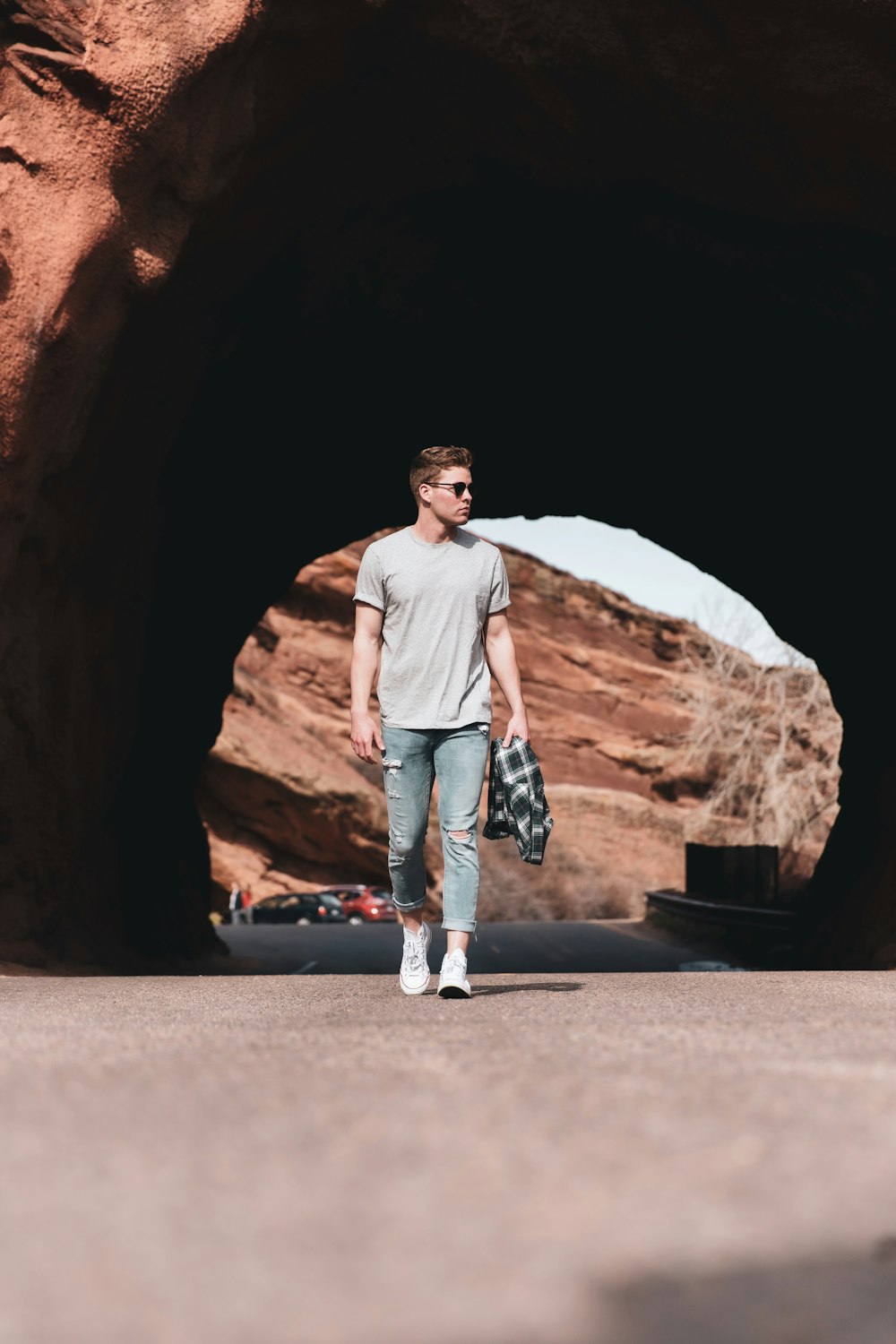 man in white crew neck t-shirt and blue denim jeans standing on brown rock formation