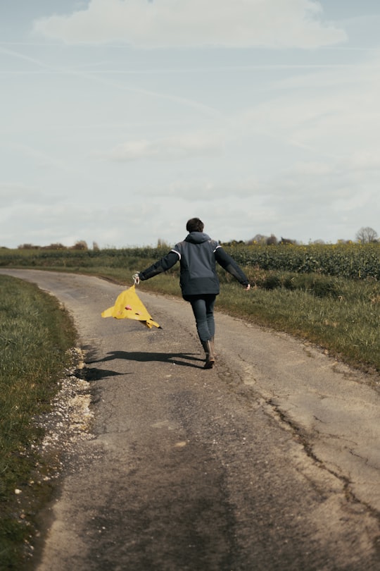 man in black jacket and blue denim jeans holding yellow umbrella walking on dirt road during in Voigny France