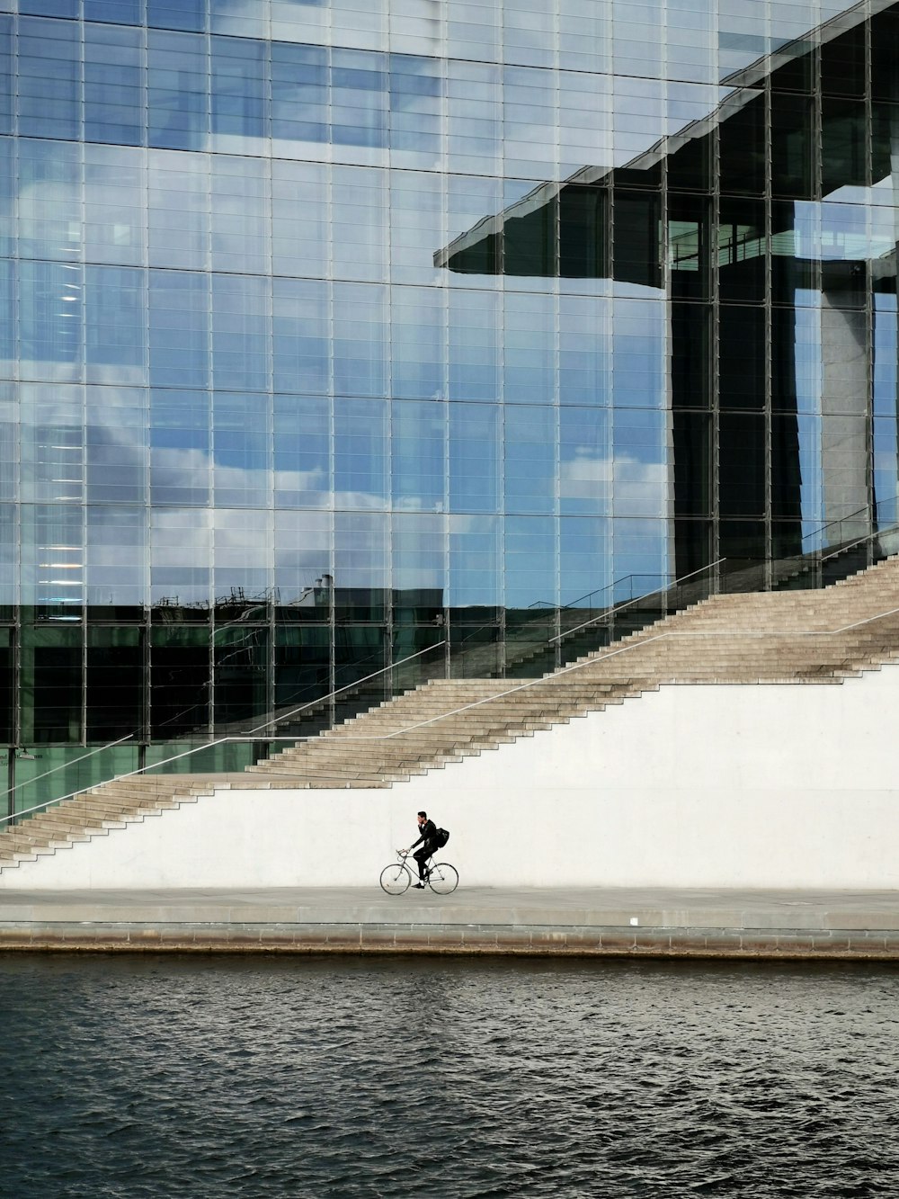 person in black jacket and black pants walking on sidewalk near glass building during daytime