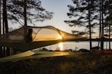 Float tent suspended between trees over rocky terrain at sunset.