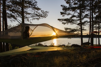 Float tent suspended between trees over rocky terrain at sunset.