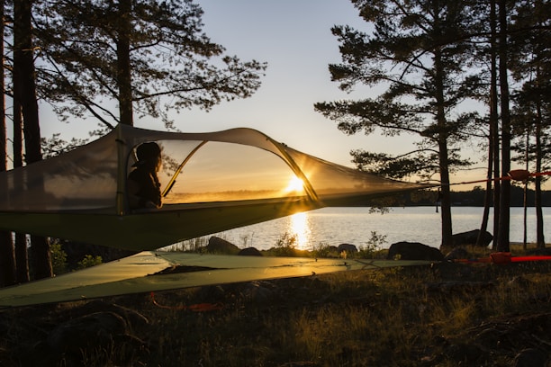 Float tent suspended between trees above a rocky forest floor at sunset.