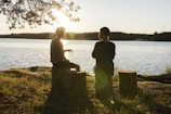 man in black jacket standing beside body of water during sunset