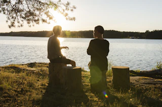 man in black jacket standing beside body of water during sunset