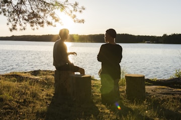 man in black jacket standing beside body of water during sunset