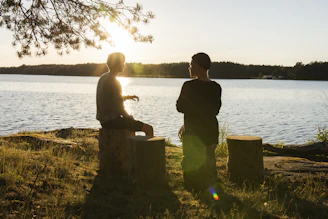 man in black jacket standing beside body of water during sunset
