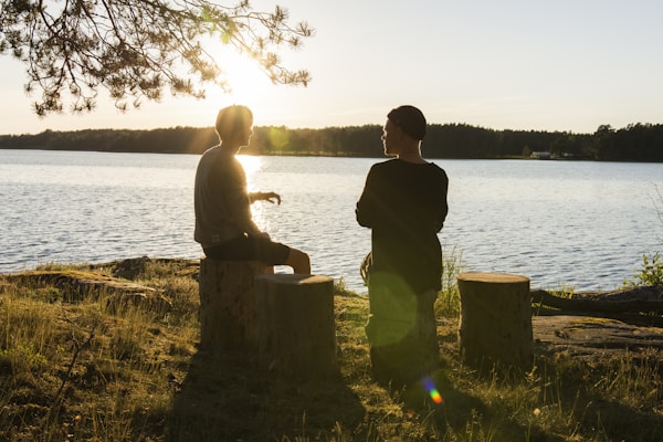 Holistic coach and client talking in nature by a lake under a tree