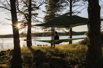 man in red shirt standing on green hammock near body of water during daytime