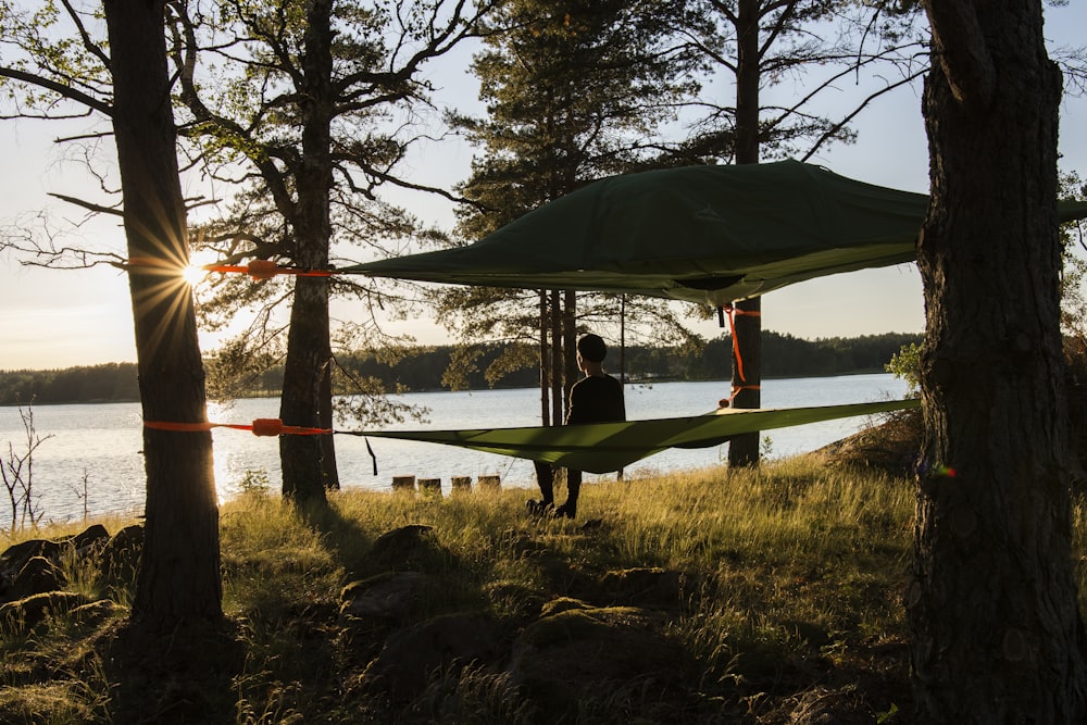 man in red shirt standing on green hammock near body of water during daytime