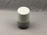 A minimalist smart speaker with soft beige casing on a white marble surface.
