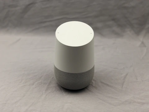 Modern smart speaker placed on a minimalist wooden table in a bright room.