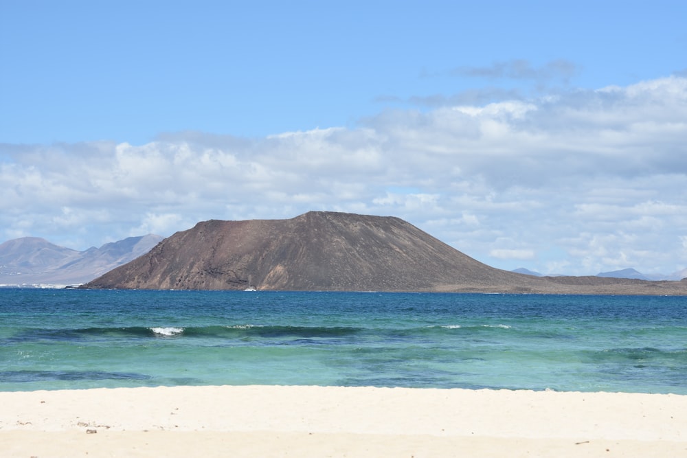 green mountain beside blue sea under blue sky during daytime