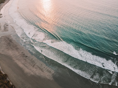A calm ocean wave gently rolling onto a sandy shore at sunset.