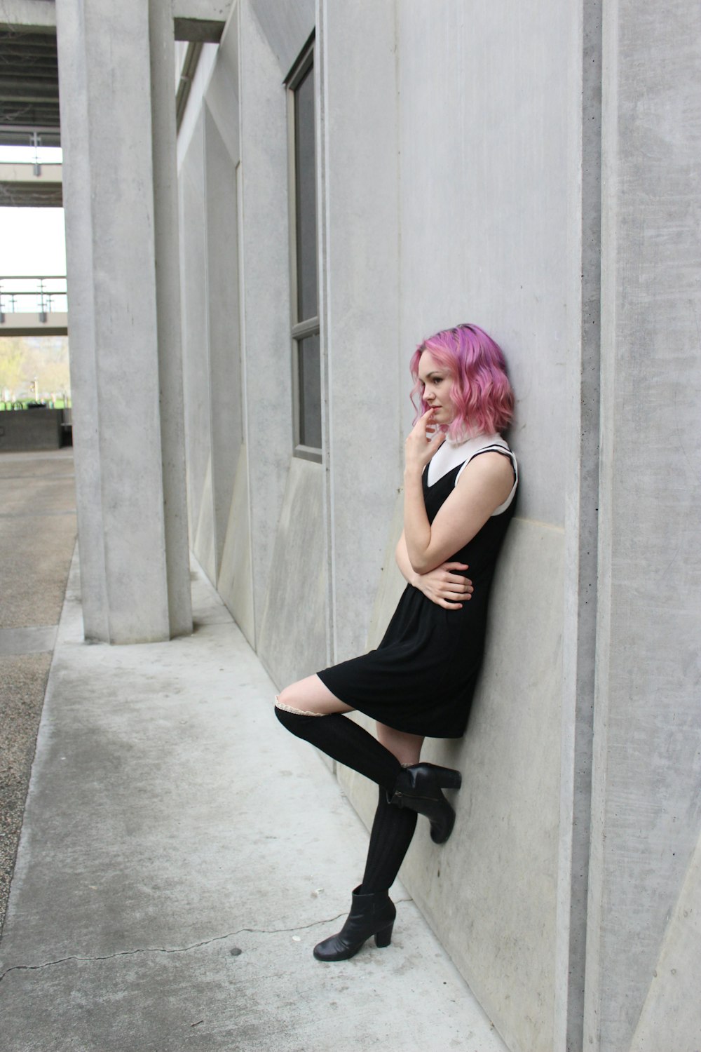 woman in black tank top and black leggings leaning on gray concrete wall