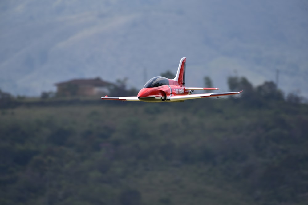 red and white airplane flying over green mountains during daytime