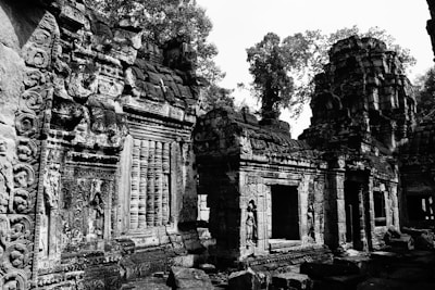An ancient stone temple with intricate carvings and weathered architecture. The structure features columns, arches, and sculpted details that showcase historical and artistic craftsmanship. Surrounded by trees, the temple exudes a sense of timelessness and mystery.