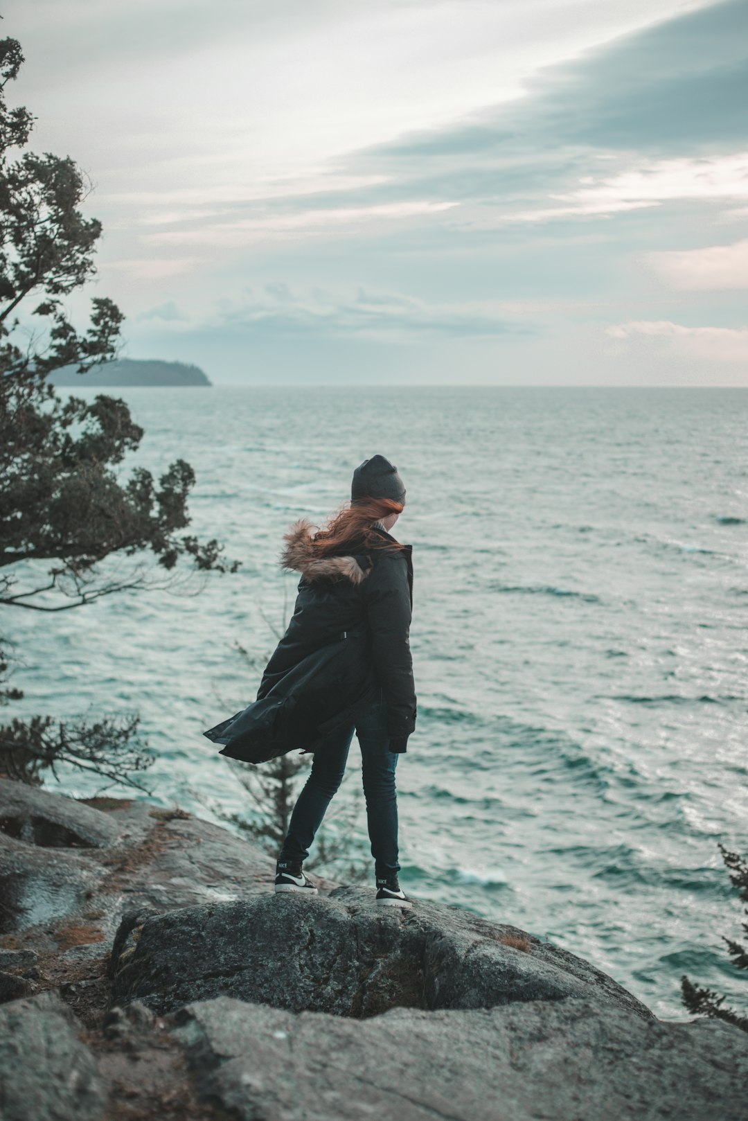 woman in black jacket standing on rock near body of water during daytime