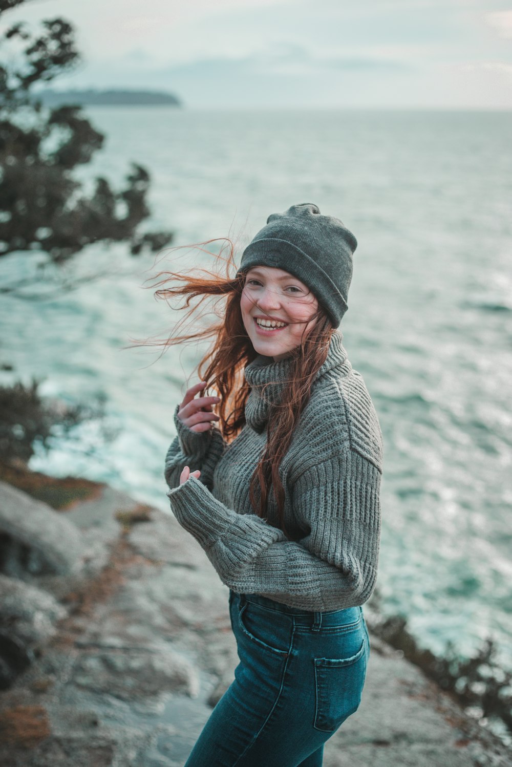 woman in gray knit sweater and blue denim jeans standing near body of water during daytime