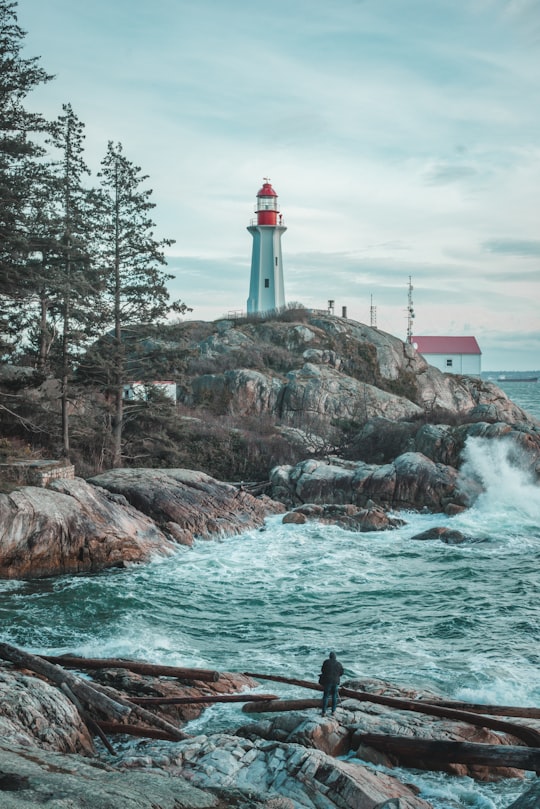 white and red lighthouse on brown rock formation near body of water during daytime in Lighthouse Park | West Vancouver Canada