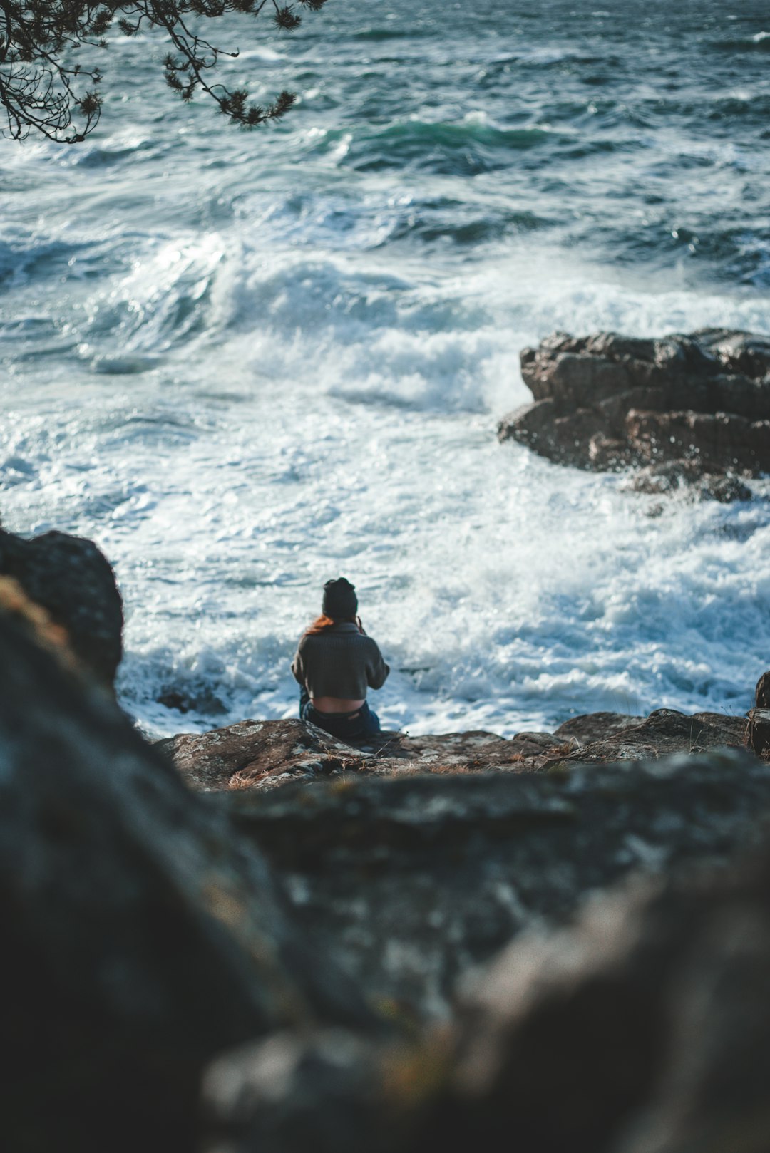 man in black shirt sitting on rock near sea during daytime