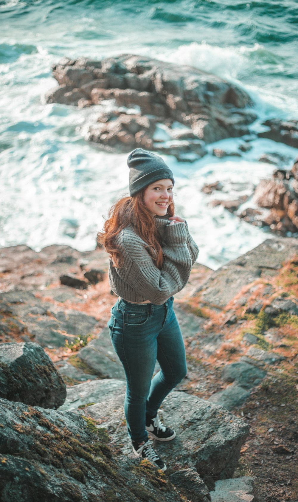 woman in brown and white striped long sleeve shirt and blue denim jeans standing on rocky