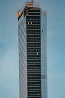A sleek navy and gold high-rise building under construction against a clear sky