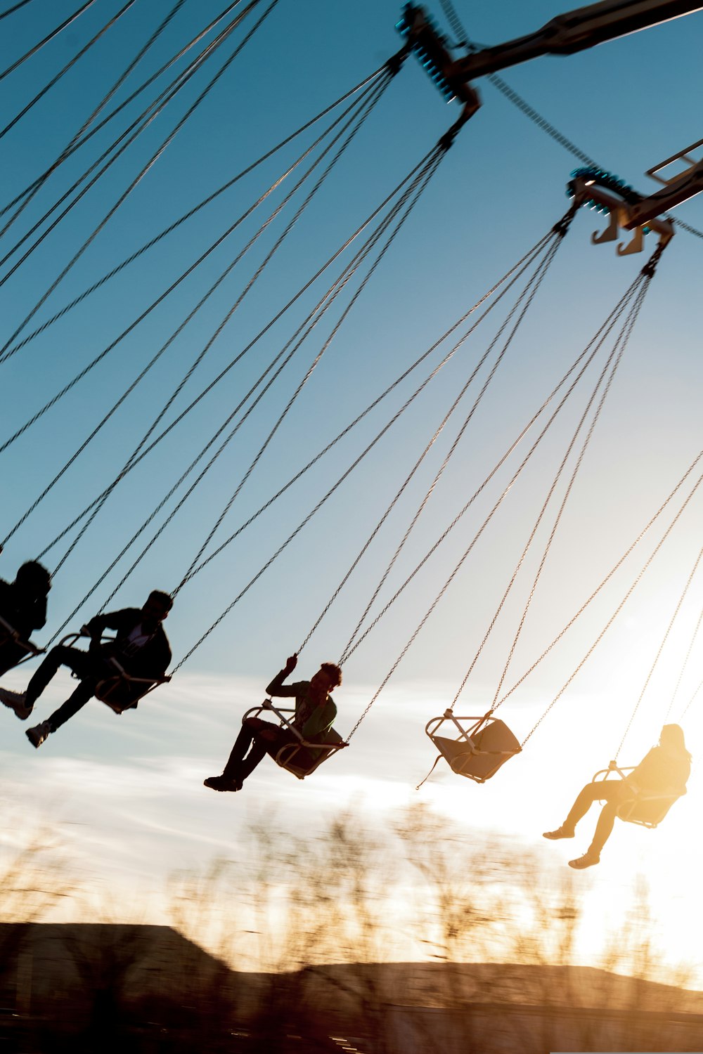 silhouette of people riding swing during daytime
