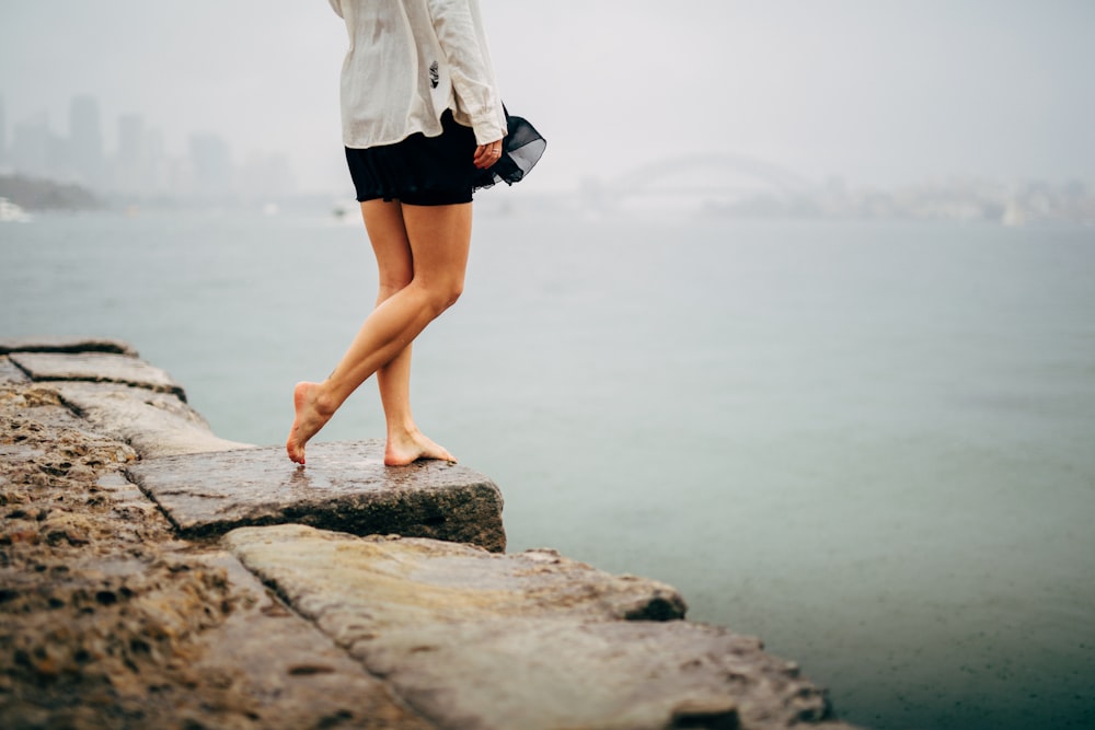 woman in white long sleeve shirt and black skirt standing on gray concrete dock during daytime