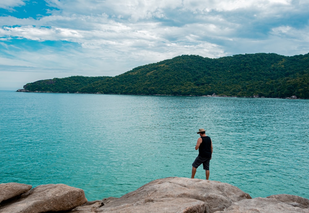 man in black shirt standing on rock near body of water during daytime