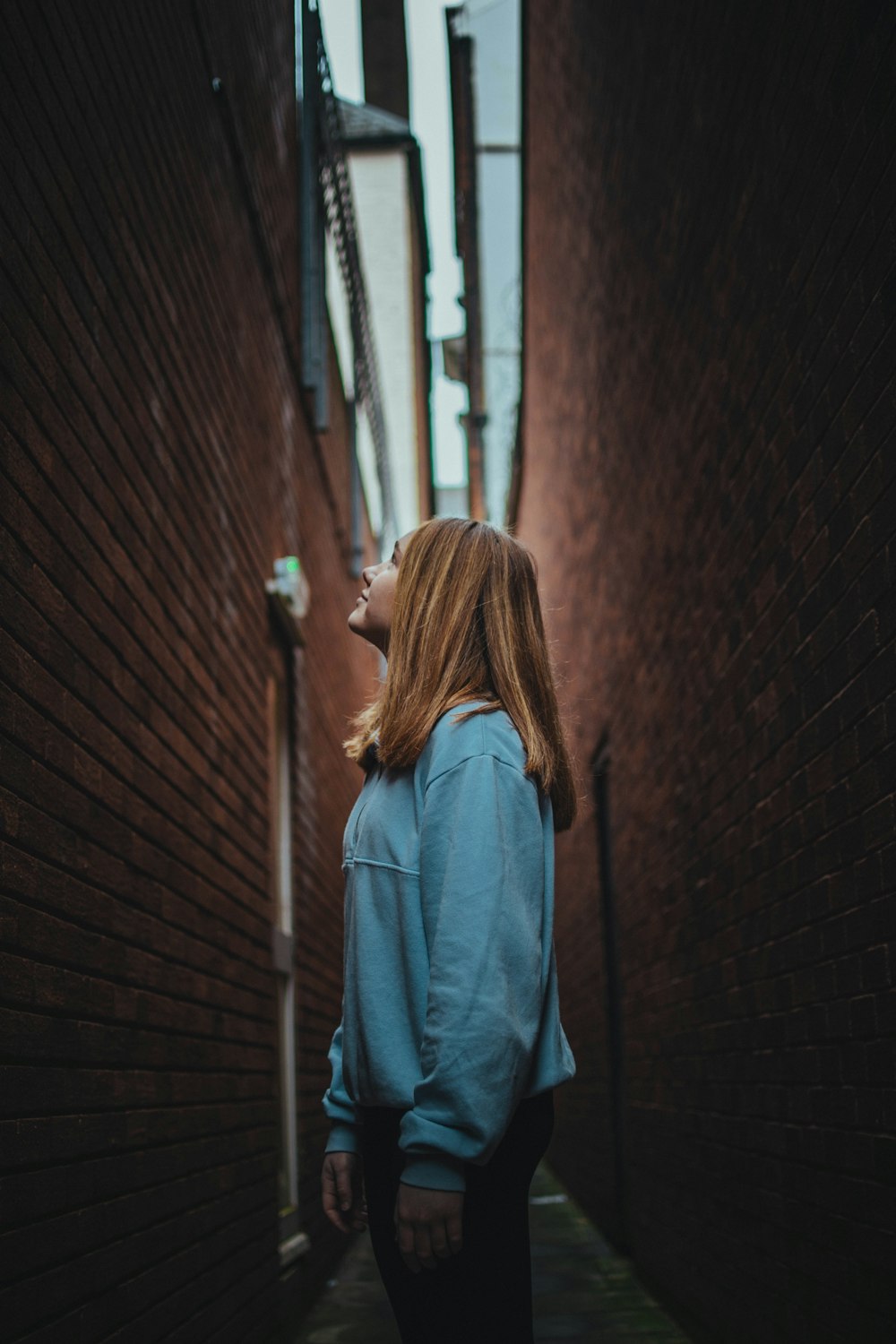 Femme en veste en jean bleue debout à côté d’un mur de briques pendant la journée